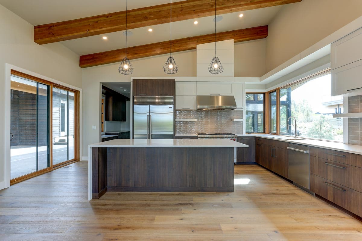 Kitchen with vaulted ceiling, exposed beams, island, stainless steel appliances, and large windows.