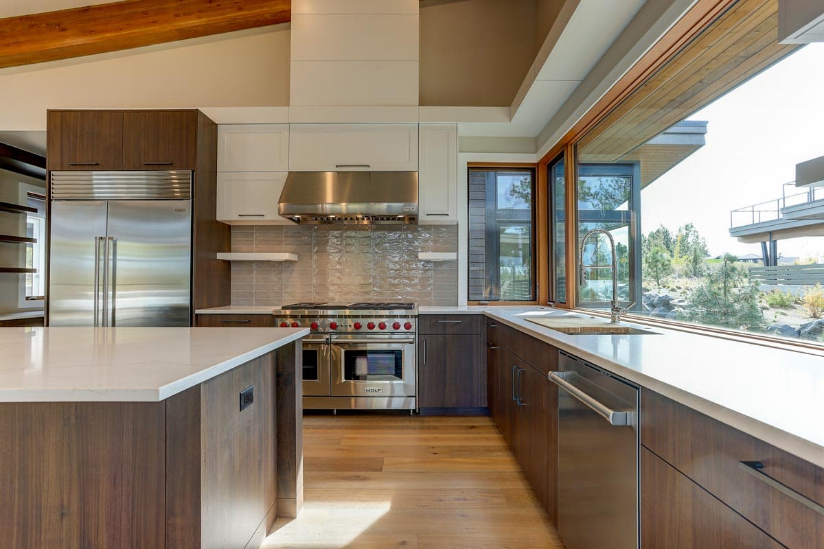 Modern kitchen with large island, stainless steel appliances, contemporary cabinetry, and a long counter with a sink below a panoramic window.