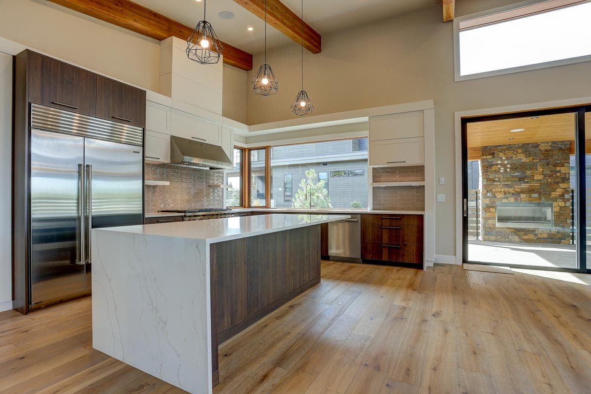 Modern kitchen with a large island, stainless steel appliances, vaulted ceiling with exposed beams, and view to outdoor fireplace.