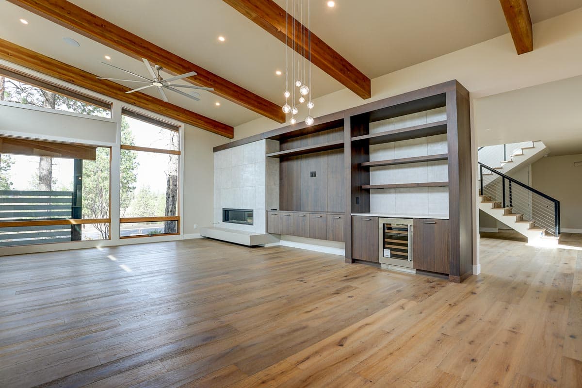 Living room with fireplace, built-in cabinetry, wood beams on vaulted ceiling, large windows, and stairs to upper level.