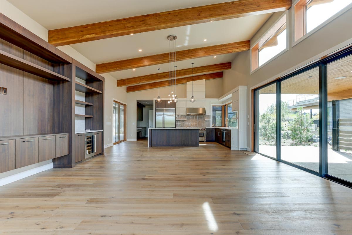 Open concept living area with vaulted beamed ceiling, kitchen island, and large sliding glass doors to exterior.