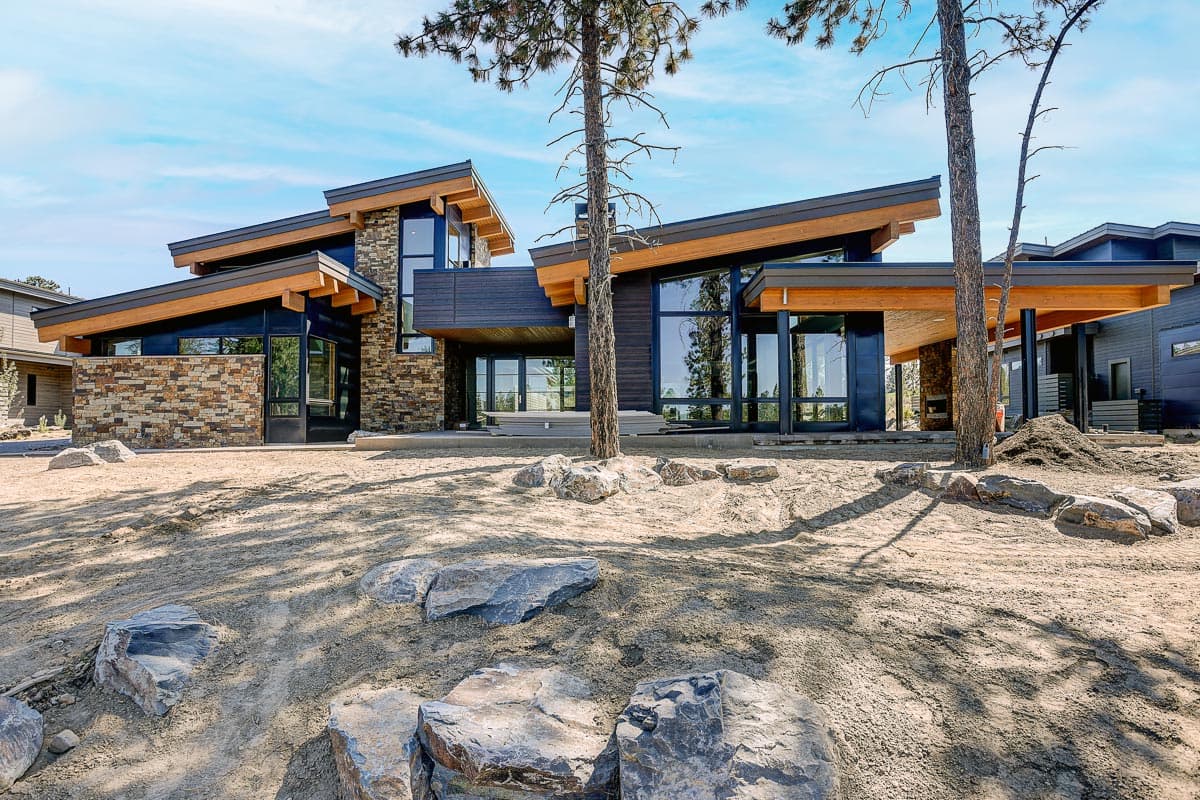 Modern house plan exterior with angled rooflines, stone and dark siding, and large glass windows.