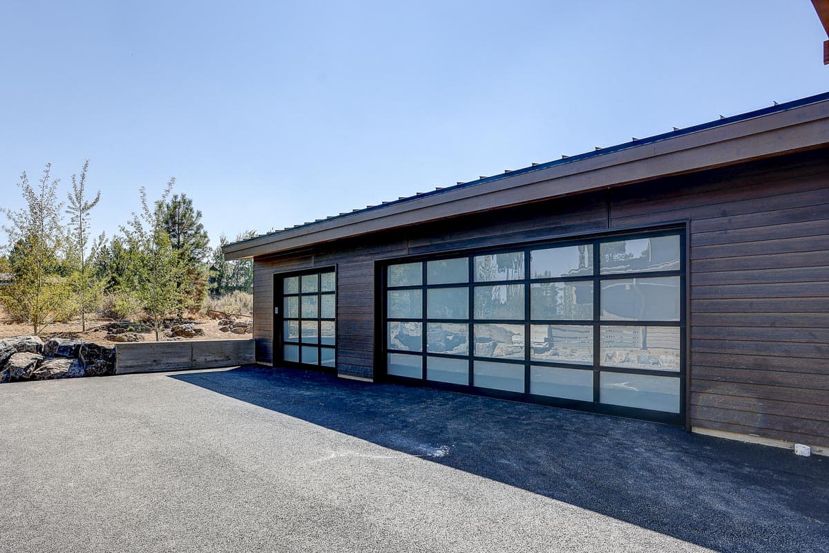 Modern house exterior with dark wood siding and two glass panel garage doors. Low-slope roofline.