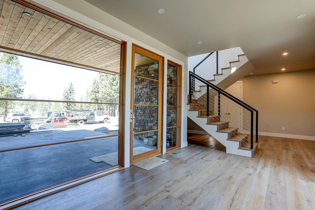Modern house interior with large windows, wood-paneled ceiling, stone accent wall, and a contemporary staircase with metal railings.