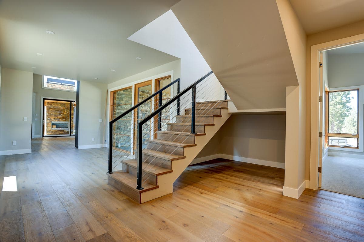 Interior view of house plan with open layout, wooden floors, modern staircase with cable railings, and stone accent wall visible through doorway.