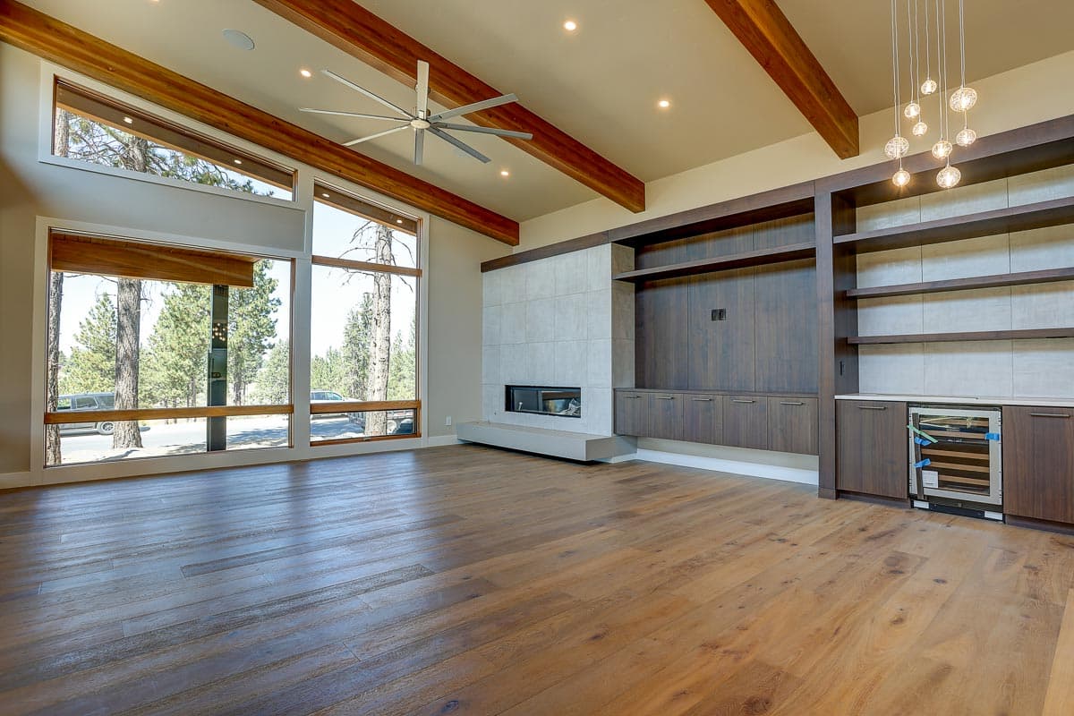 Interior rendering of a great room with vaulted ceilings, exposed beams, large windows, a modern fireplace, and built-in shelving.