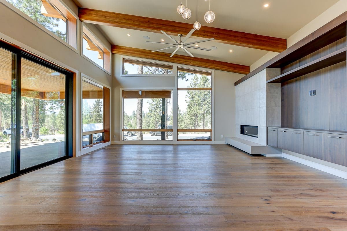 Modern living room with vaulted wood beam ceiling, large windows, fireplace, and built-in media center.
