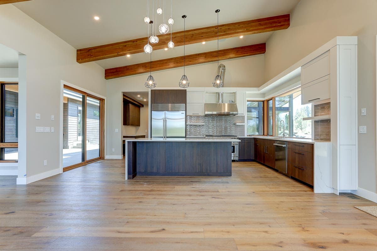 Modern kitchen with island, stainless steel appliances, vaulted ceiling with exposed beams, and large windows.