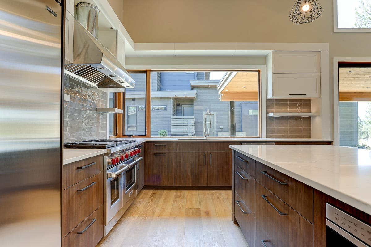 Contemporary kitchen with large island, stainless steel range, wood cabinetry, and a wide window overlooking modern homes.
