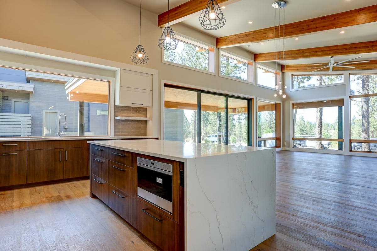 Modern kitchen with waterfall island, wood cabinetry, and vaulted ceiling with exposed beams and large windows.