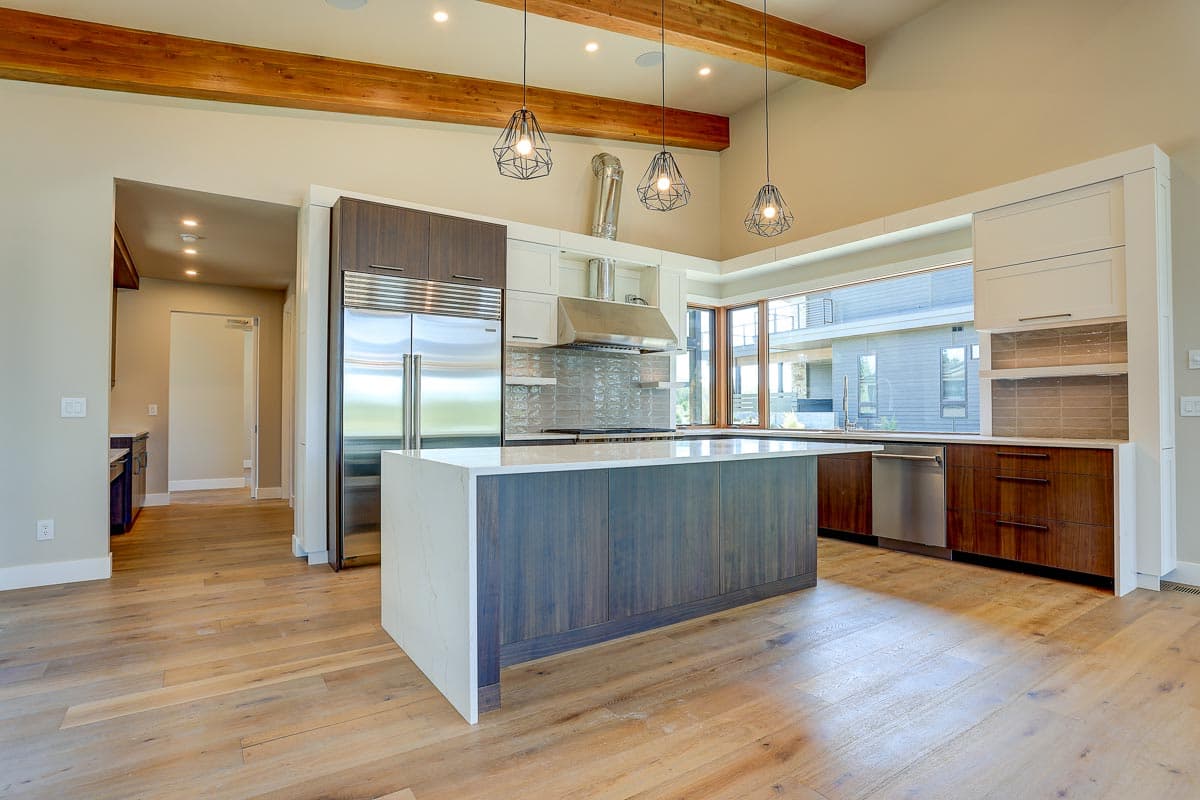 Modern kitchen with island, stainless steel appliances, vaulted ceiling with exposed beams, and large windows.
