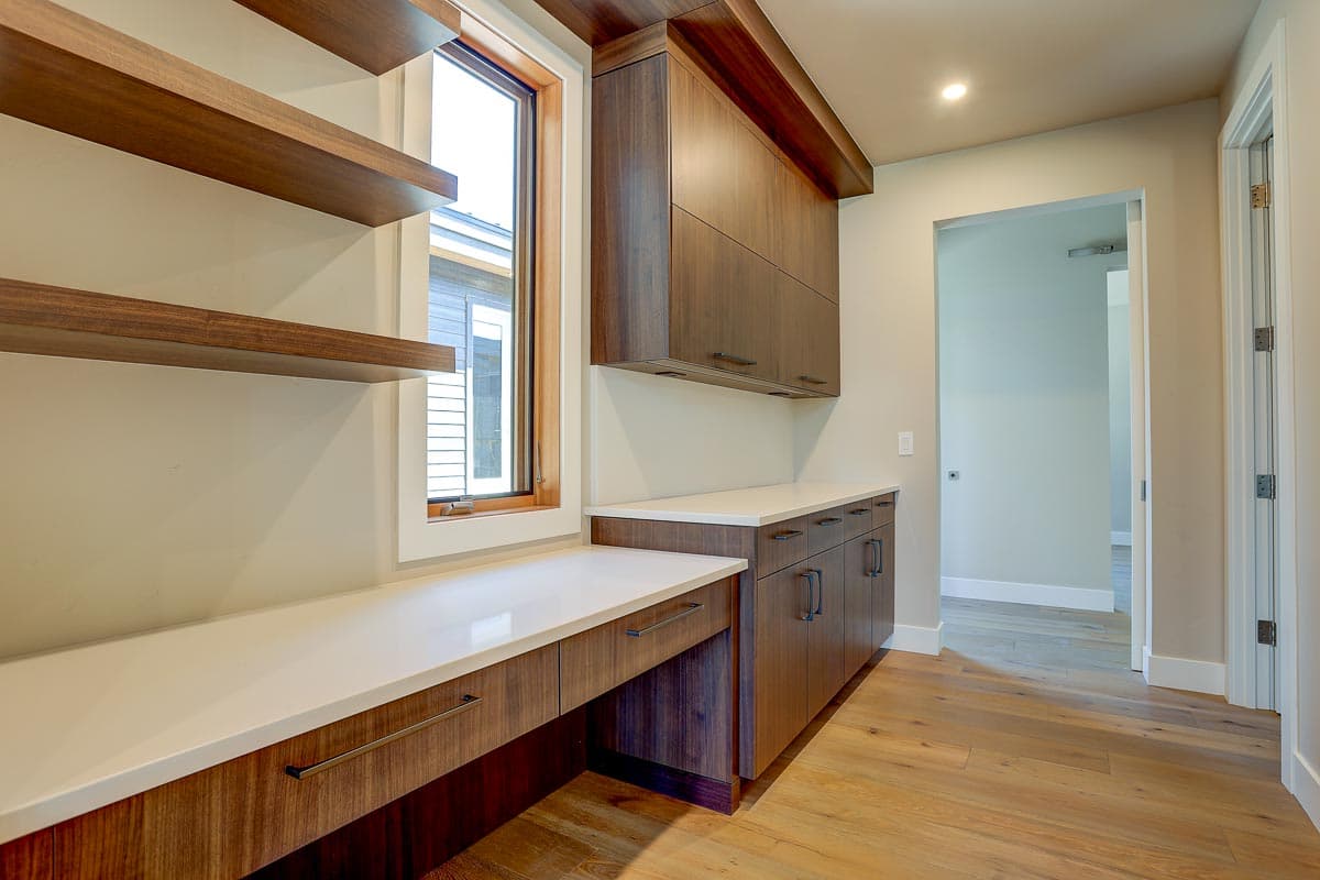 Interior view of a home office with a built-in desk, floating shelves, and dark wood cabinetry. Open doorway shows hallway.