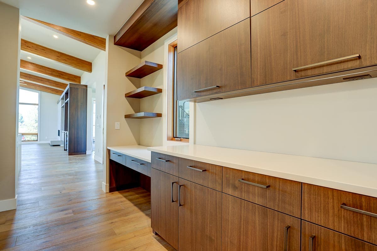 Interior view of a home office area with built-in wood cabinetry, floating shelves, and a desk.