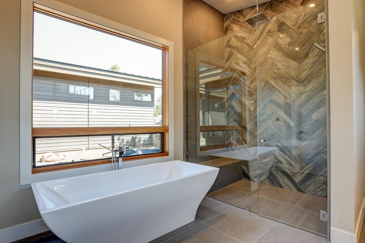 Modern bathroom with freestanding tub and glass-enclosed shower featuring herringbone tile and rainfall showerhead.
