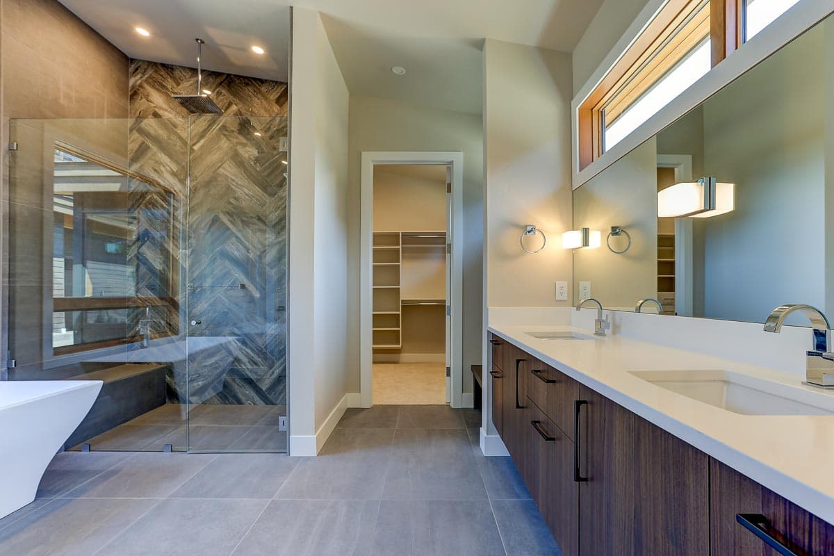 Modern bathroom with walk-in closet, double vanity, and glass-enclosed shower with patterned tile.