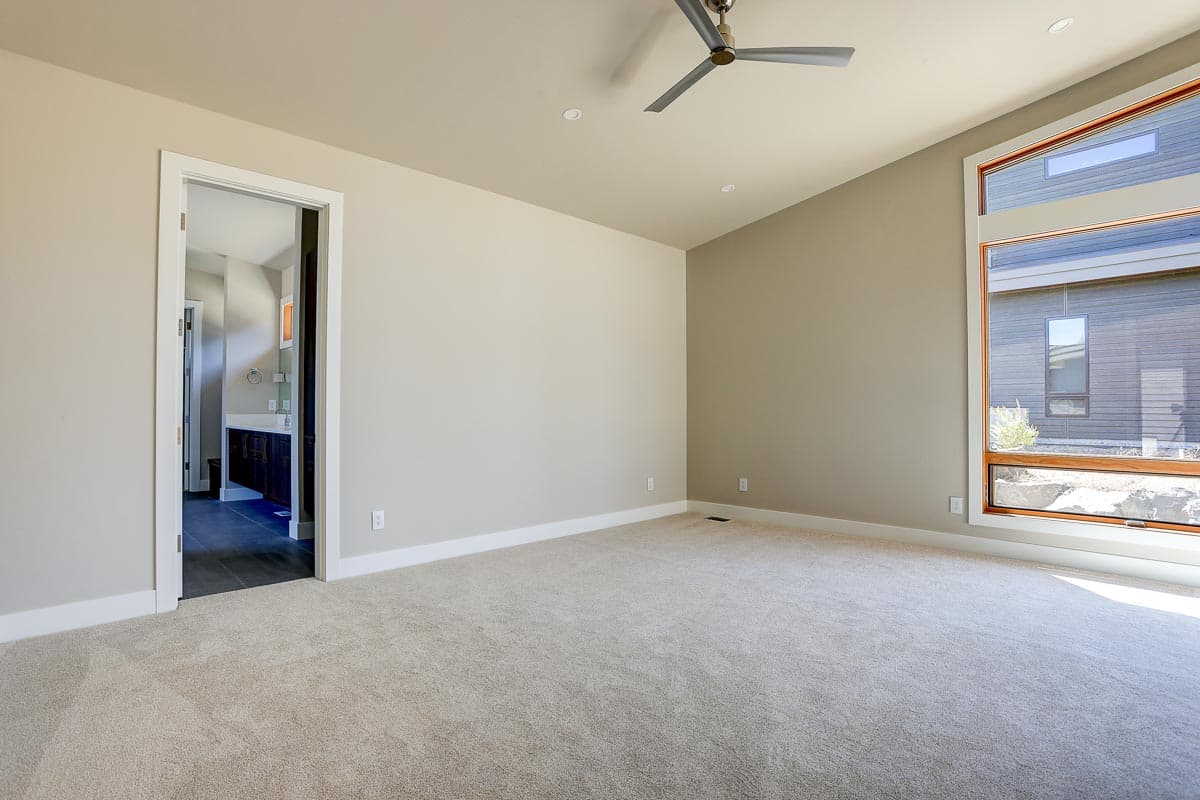 Interior view of a spacious bedroom with a ceiling fan, a large multi-pane window, and a doorway to a bathroom with a vanity.