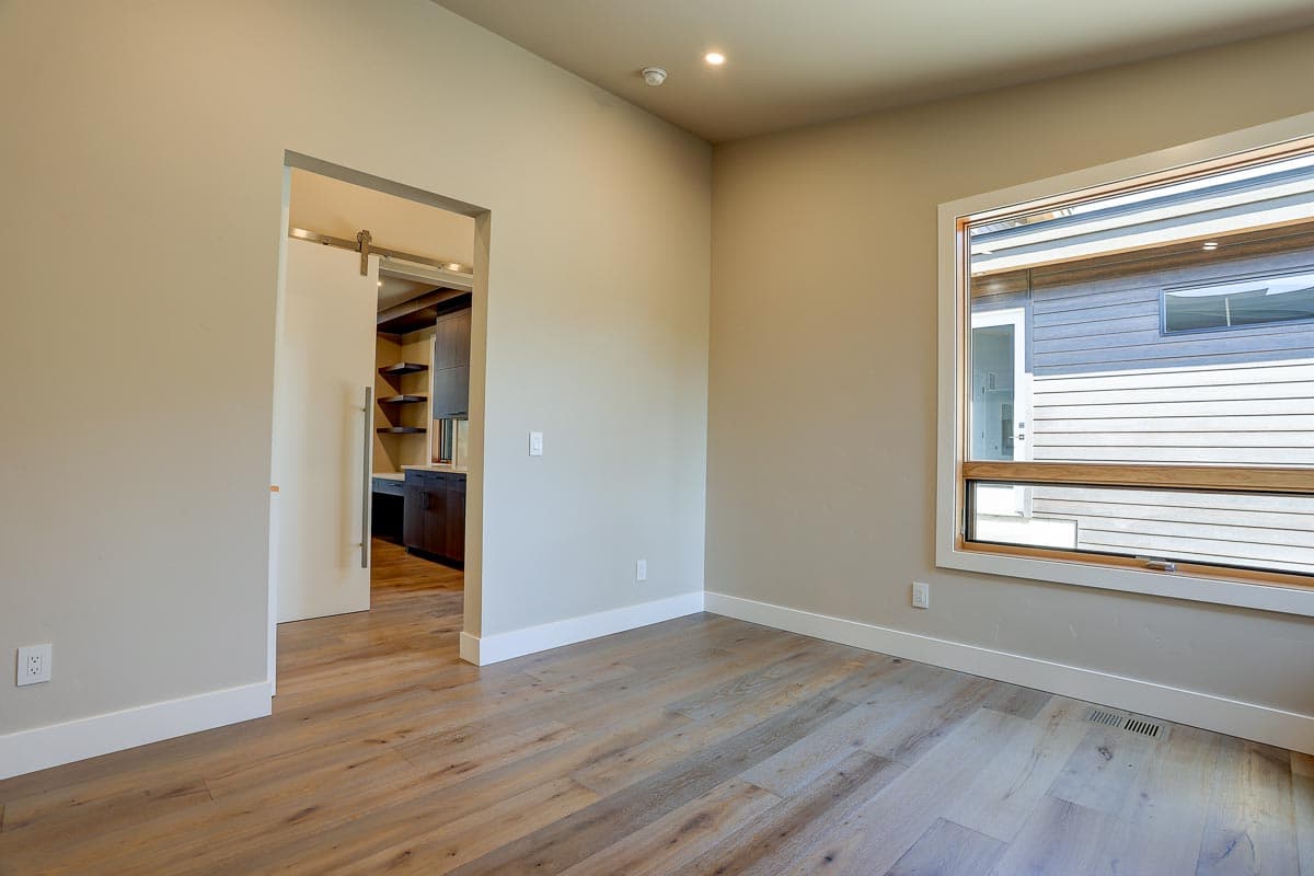 Interior view of room with wood-look flooring, sliding barn door to office with built-in shelving, and large window.