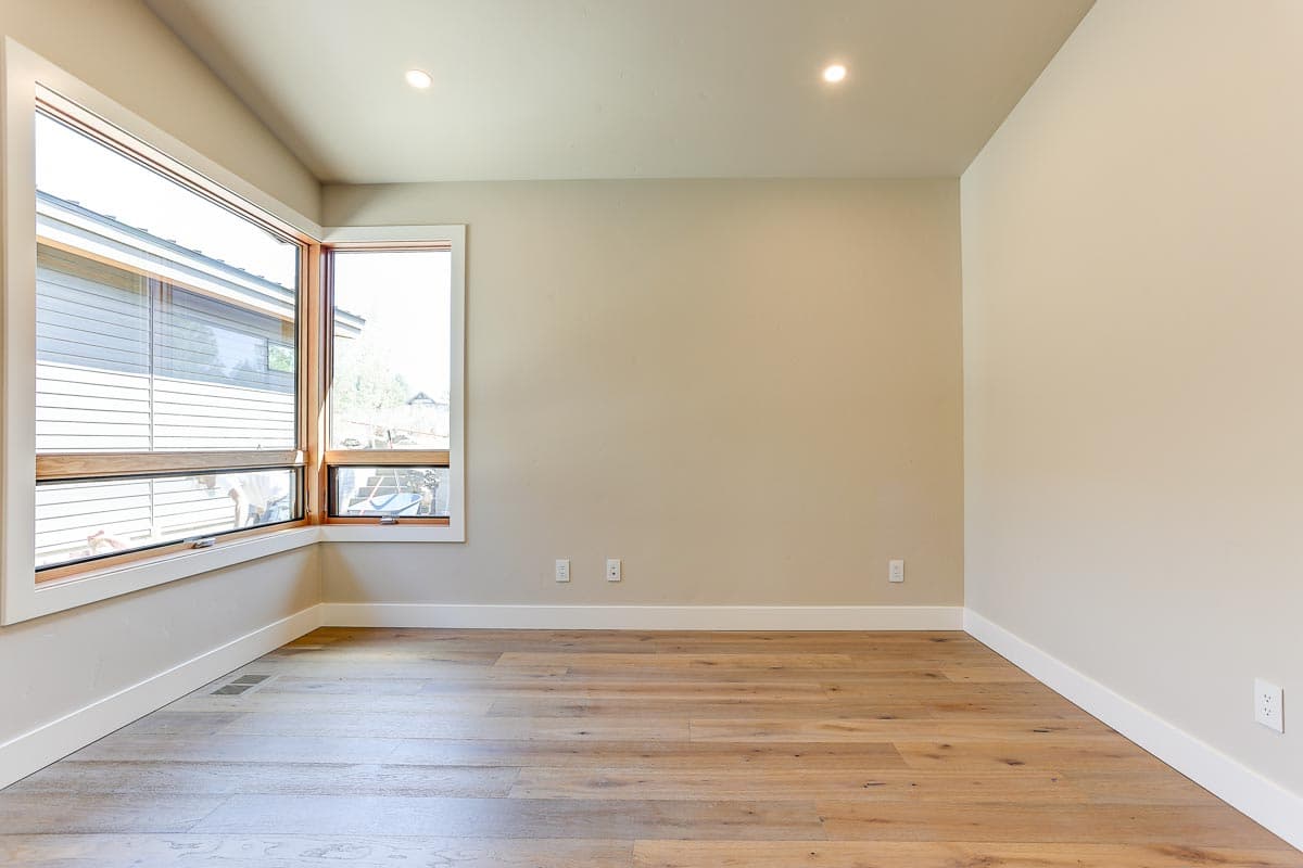 Interior view of an empty room with corner windows, light wood flooring, and recessed lighting.
