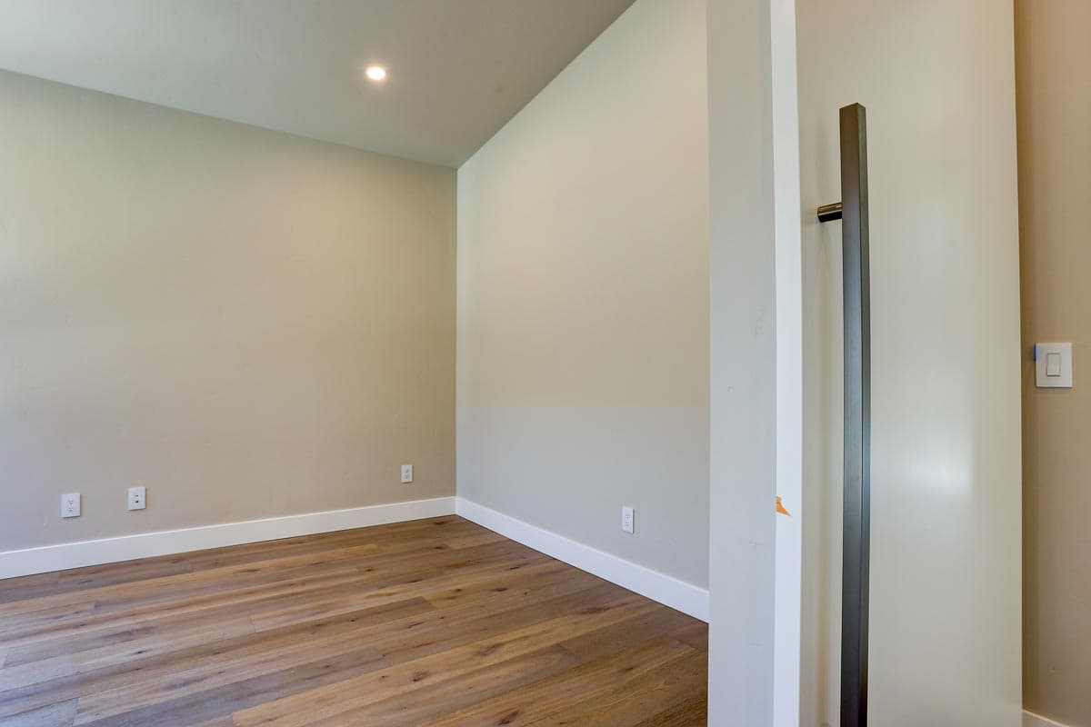 Interior view of a room with light neutral walls, white baseboards, wood flooring, recessed lighting, and a tall dark door pull.