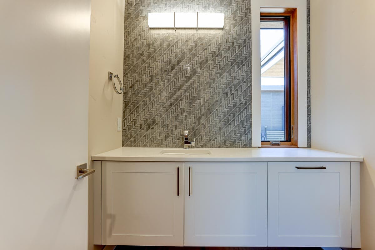 Powder room vanity with white cabinetry, quartz countertop, herringbone tile backsplash, and chrome fixtures.