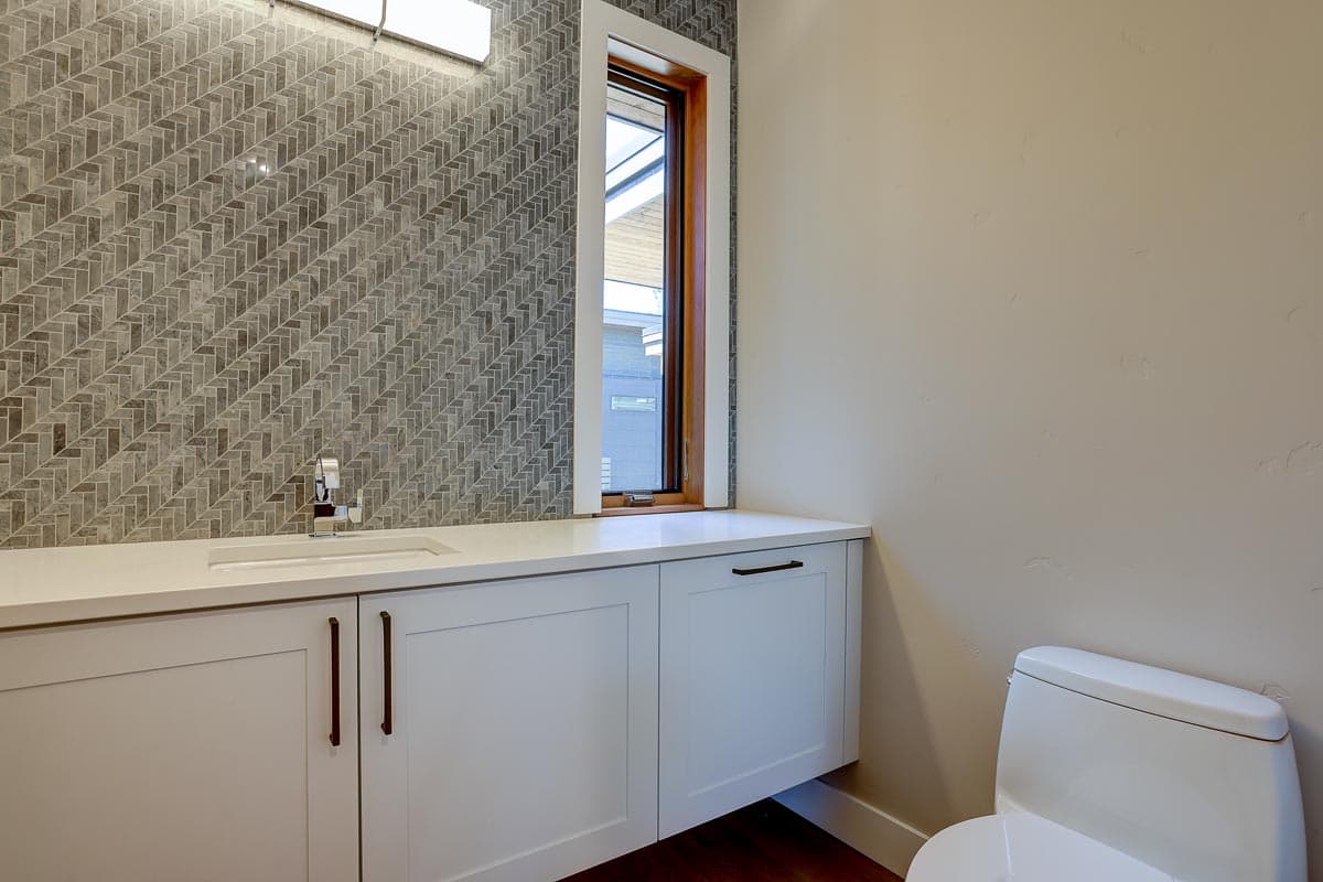 Bathroom vanity with white cabinetry, quartz countertop, sink, and herringbone tile backsplash.