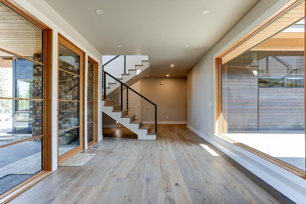 Interior view of a house plan showing a staircase with wood and stone accents, large windows, and wood flooring.