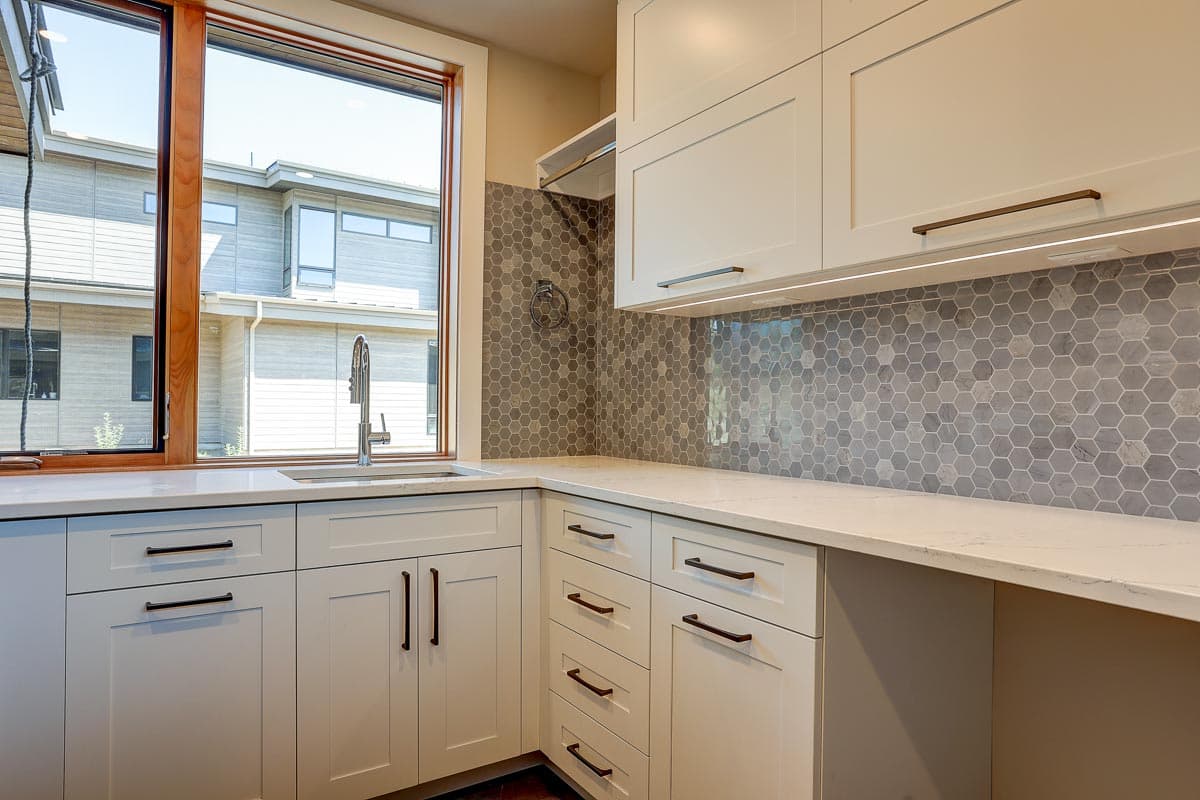Kitchen with white shaker cabinets, quartz countertops, hexagon tile backsplash, and a large window overlooking modern architecture.
