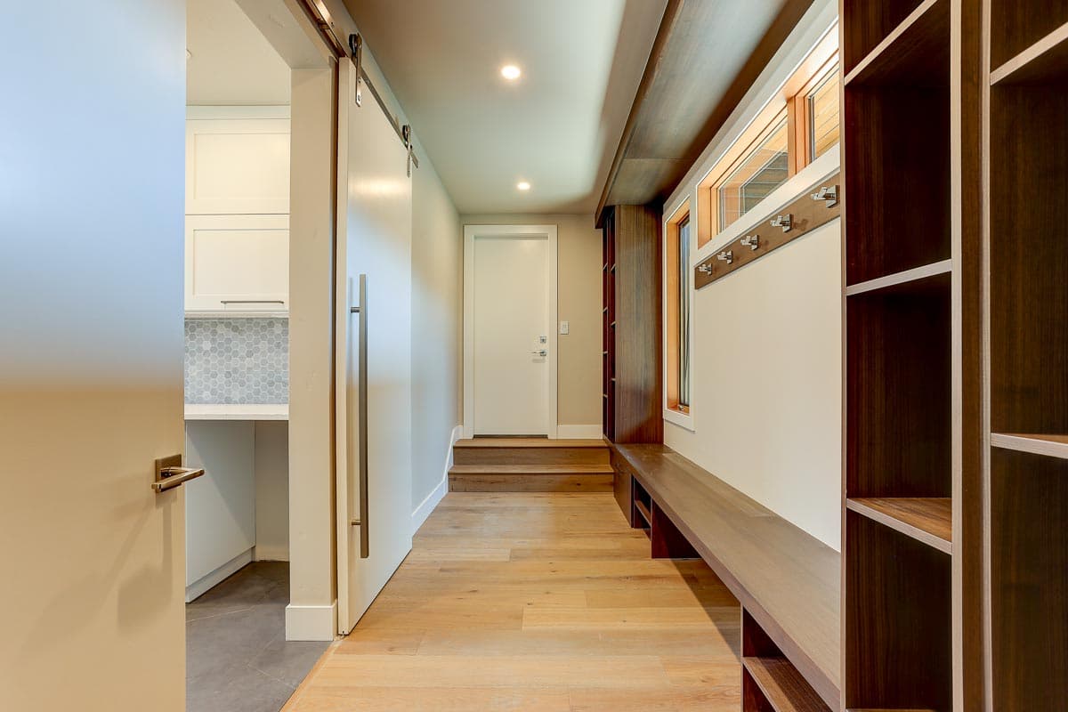 Mudroom with wood flooring, built-in bench, coat rack, and sliding barn door leading to laundry area.