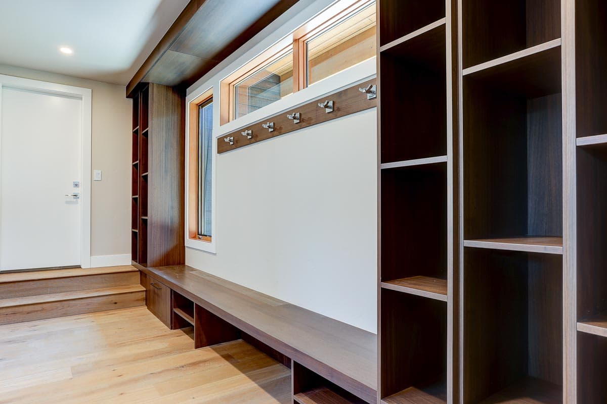 Mudroom with built-in dark wood shelving, bench seating, coat hooks, and clerestory windows.