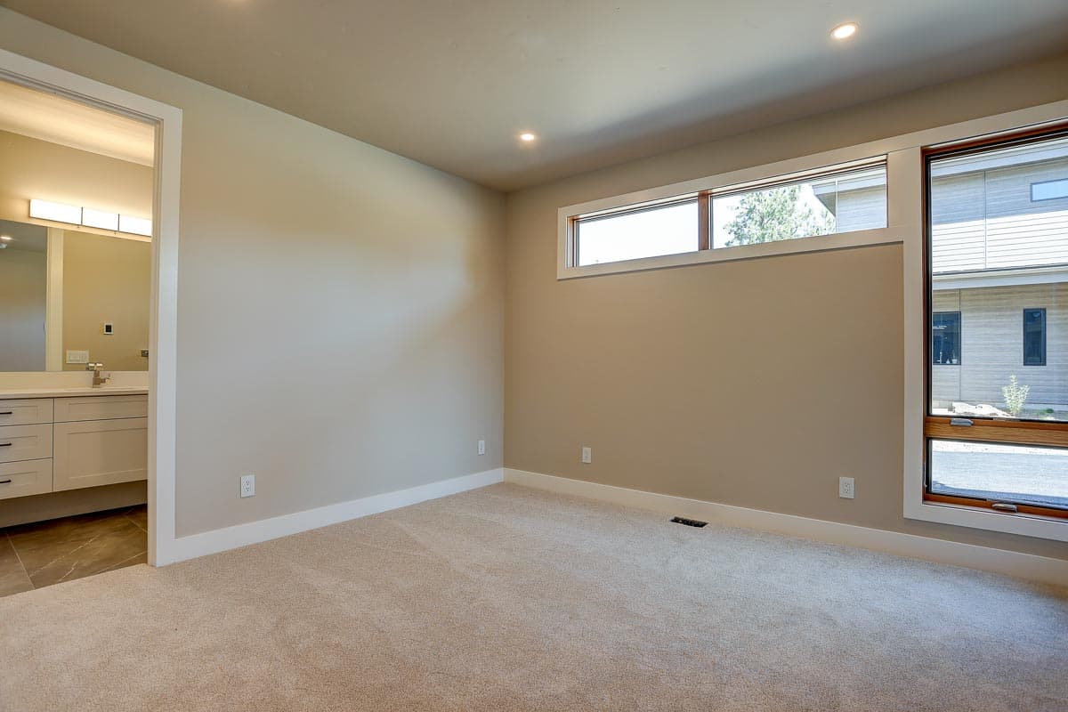 Bedroom with horizontal windows, view to modern exterior, and doorway to bathroom with vanity.