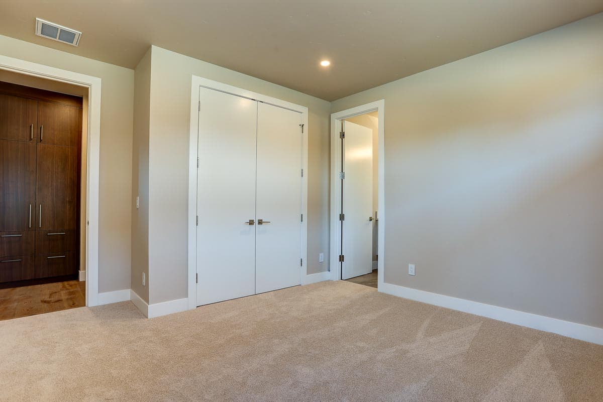 Bedroom interior with double closet doors, built-in wood cabinetry, and doorway to another room.