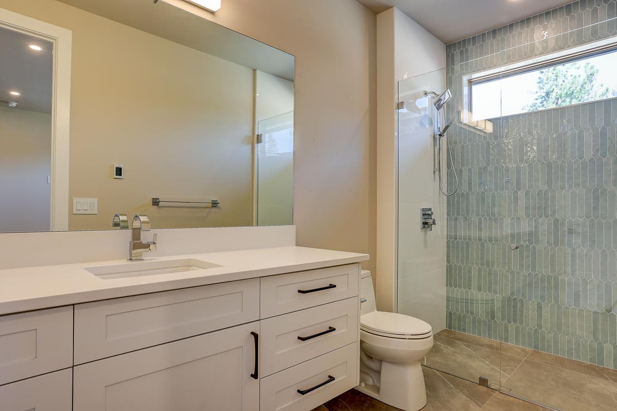 Modern bathroom with double vanity, white cabinetry, glass-enclosed shower with picket tile and horizontal window.