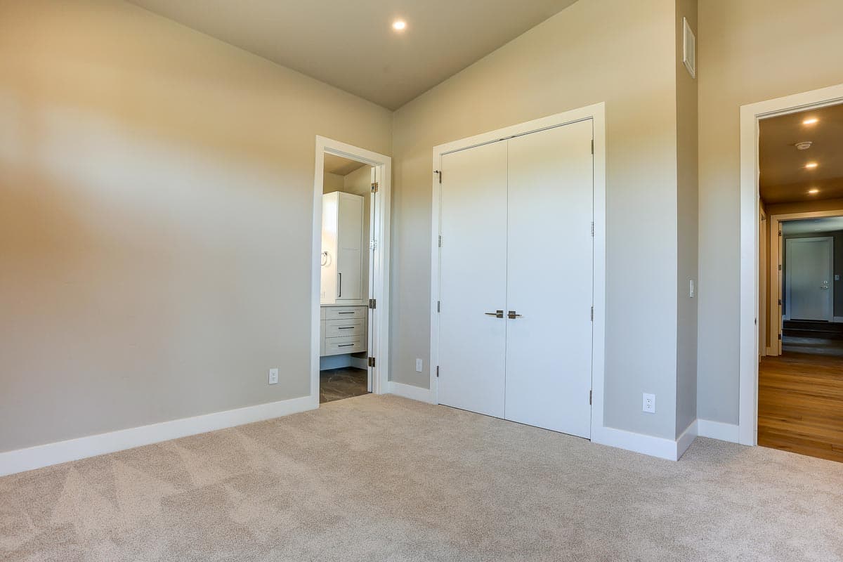 Bedroom with double closet doors, view into bathroom with vanity and cabinetry, and hallway access.