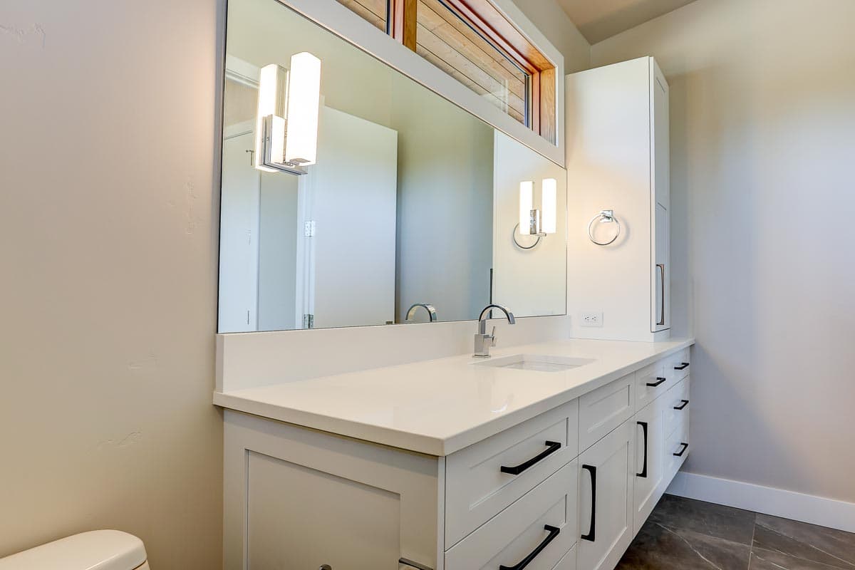 Bathroom vanity with white quartz countertop, white cabinets with black hardware, undermount sink, and long wall mirror.