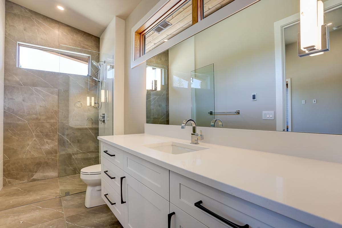 Modern bathroom with a large vanity, white quartz countertop, and a glass-enclosed shower with marble tile.