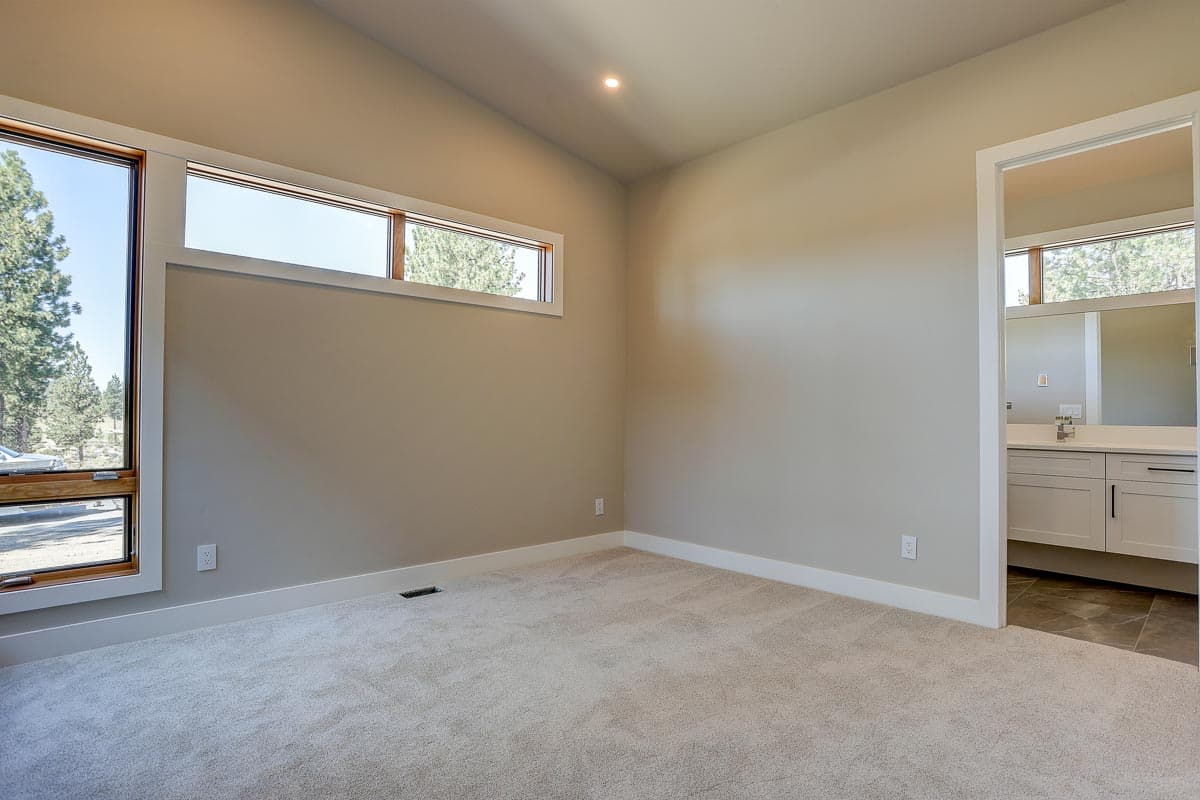 Interior view of a bedroom with sloped ceiling, horizontal windows, and doorway to a bathroom with double vanity.