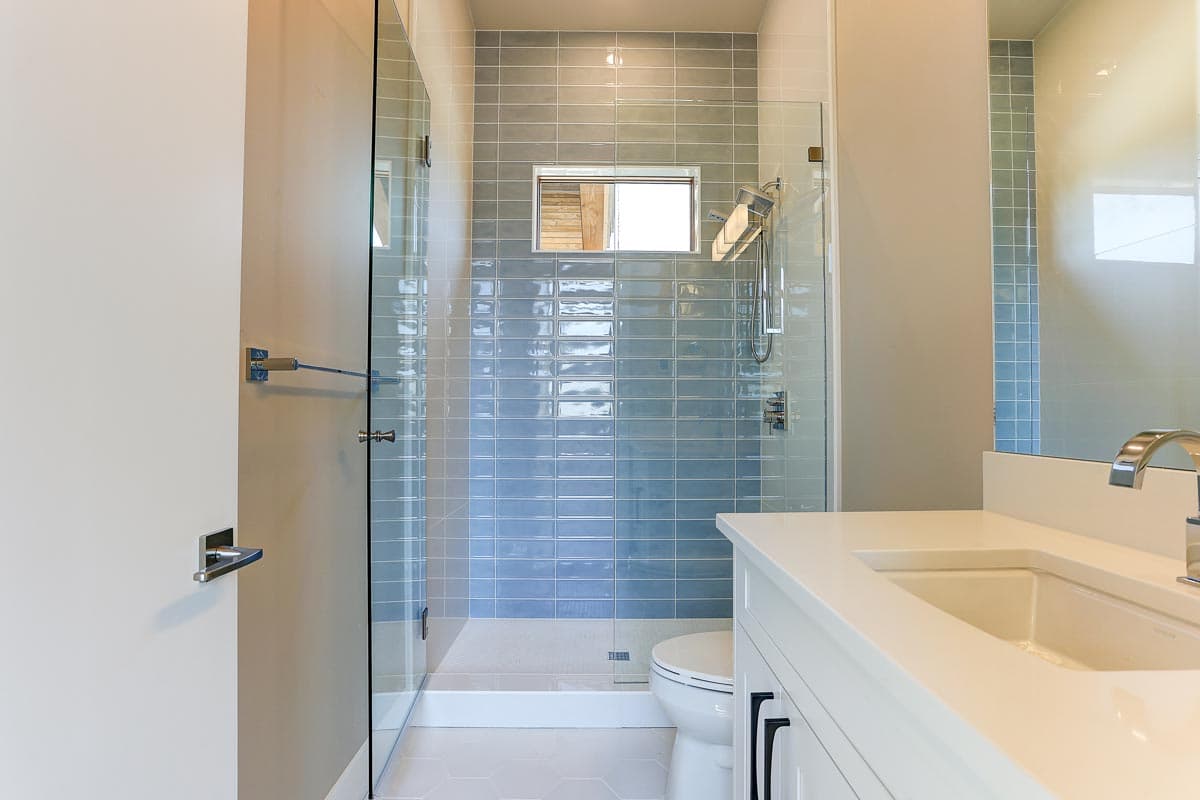 Modern bathroom with glass-enclosed shower featuring blue subway tile and a small horizontal window above the toilet.