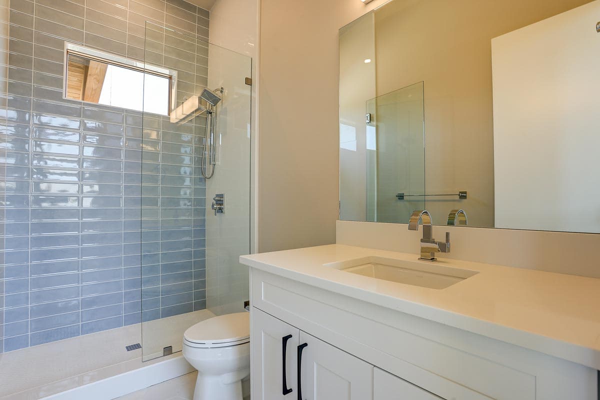Modern bathroom with glass-enclosed shower featuring blue subway tile and a white vanity with a rectangular sink and chrome faucet.