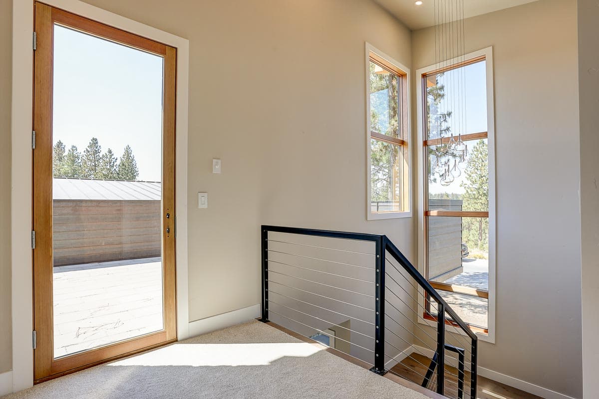 Interior view showing wooden door, cable railing staircase, and tall windows with view of trees and modern exterior.