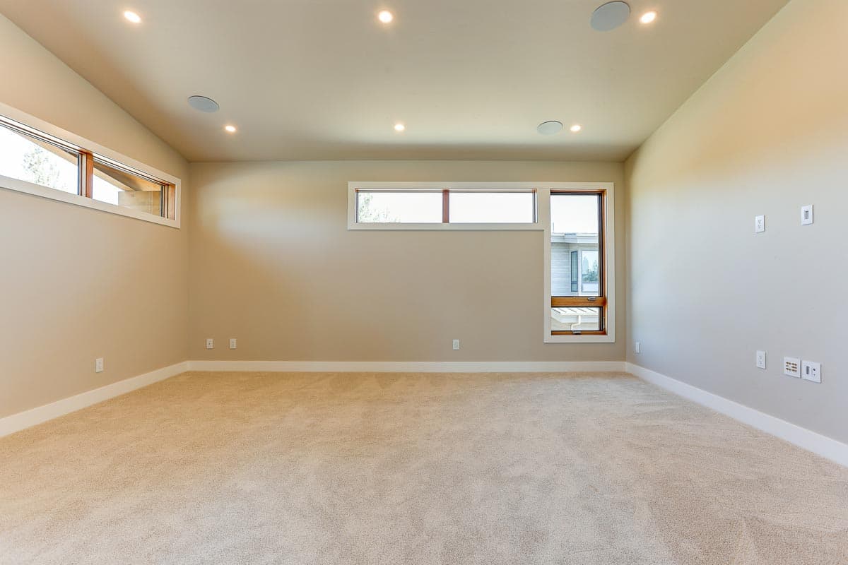 Interior view of a carpeted room with recessed lighting and horizontal windows with wood trim.