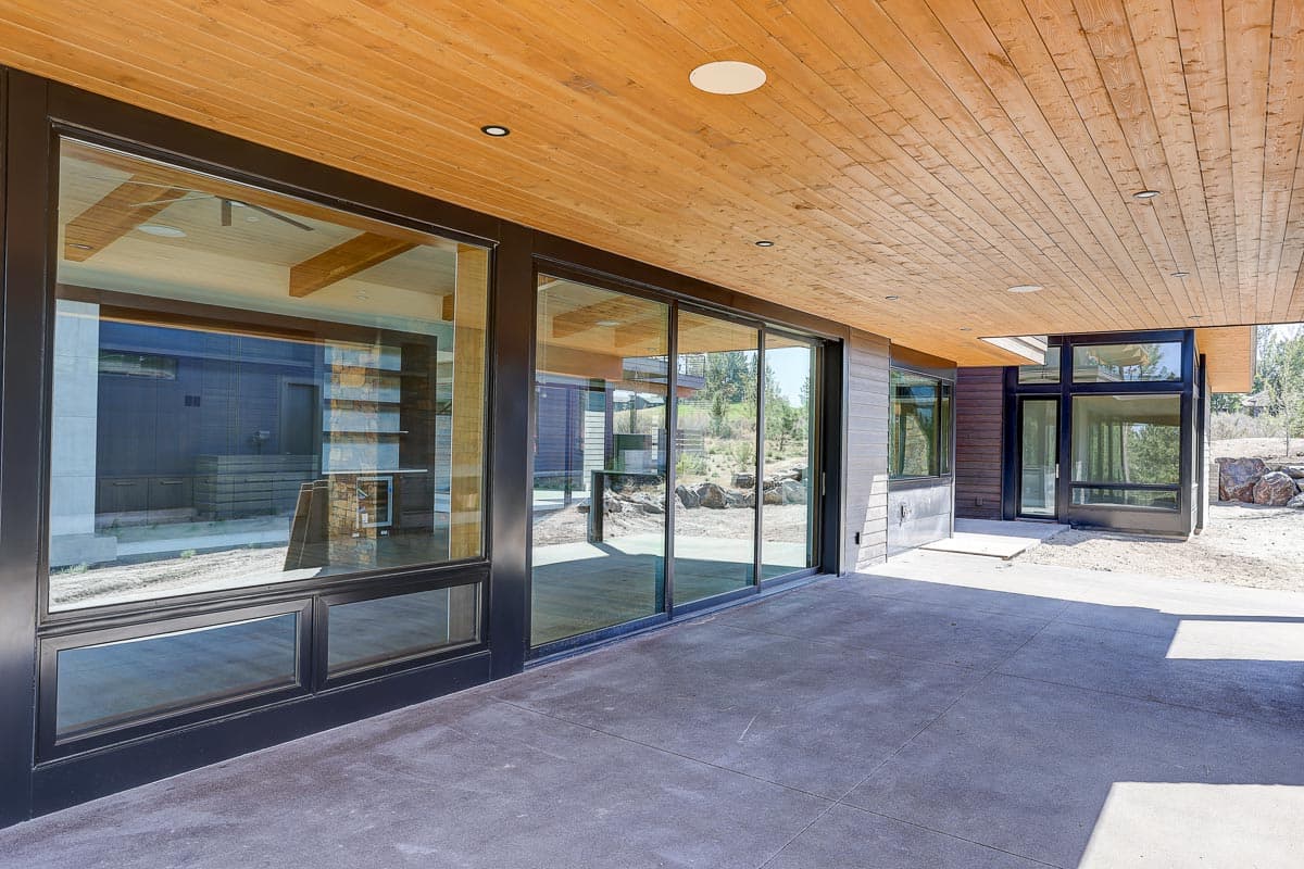 Modern house exterior with large sliding glass doors, wood plank ceiling, and dark metal trim.