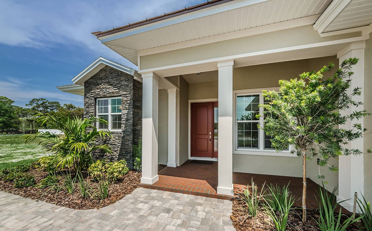 House plan exterior featuring a covered porch with columns, stone accent walls, a red front door, and multiple windows.