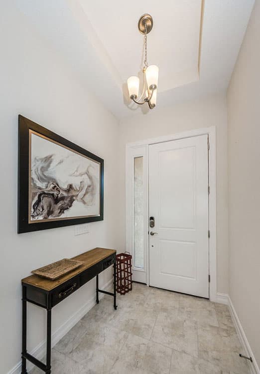 Entryway with white door, sidelight, console table, abstract art, and chandelier.