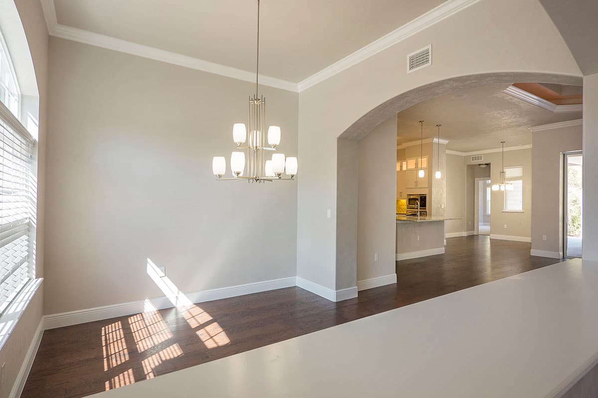 Interior view of a dining area with arched entryway to kitchen, chandelier, and large window.