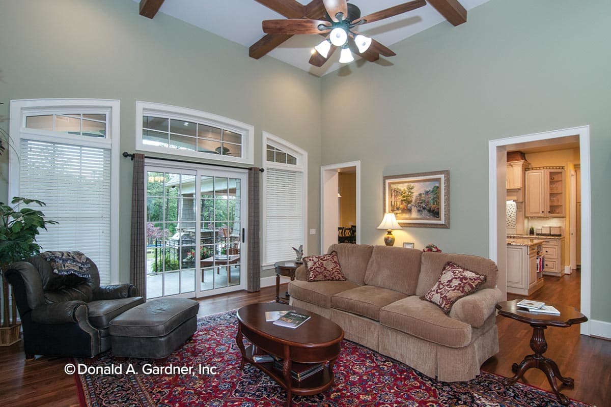 Living room with vaulted ceiling, exposed beams, fireplace, and view to kitchen. Sliding glass doors open to patio.