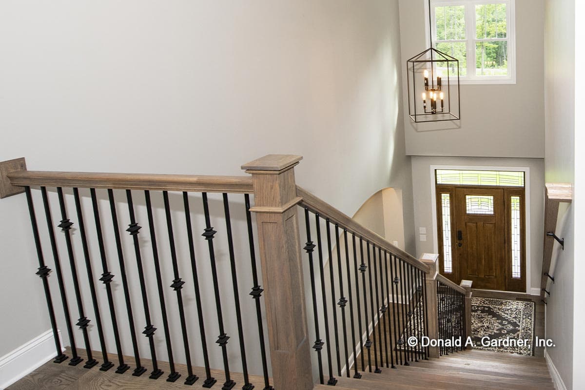 Interior view of staircase with wood banister, wrought iron spindles, and view of front door and upper window.