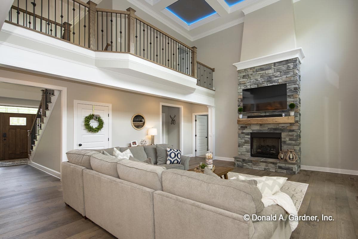Great room with stone fireplace, vaulted ceiling, loft overlook with wood and wrought iron railing, and interior entryway.