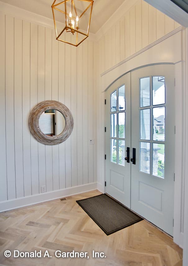 Interior view of a foyer with double glass doors, shiplap walls, herringbone hardwood floors, and a geometric lantern.