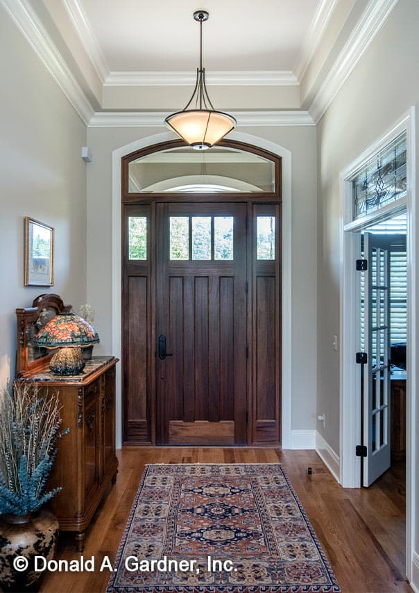 Foyer interior with paneled wooden door, arched transom window, ornate chandelier, and Persian rug.