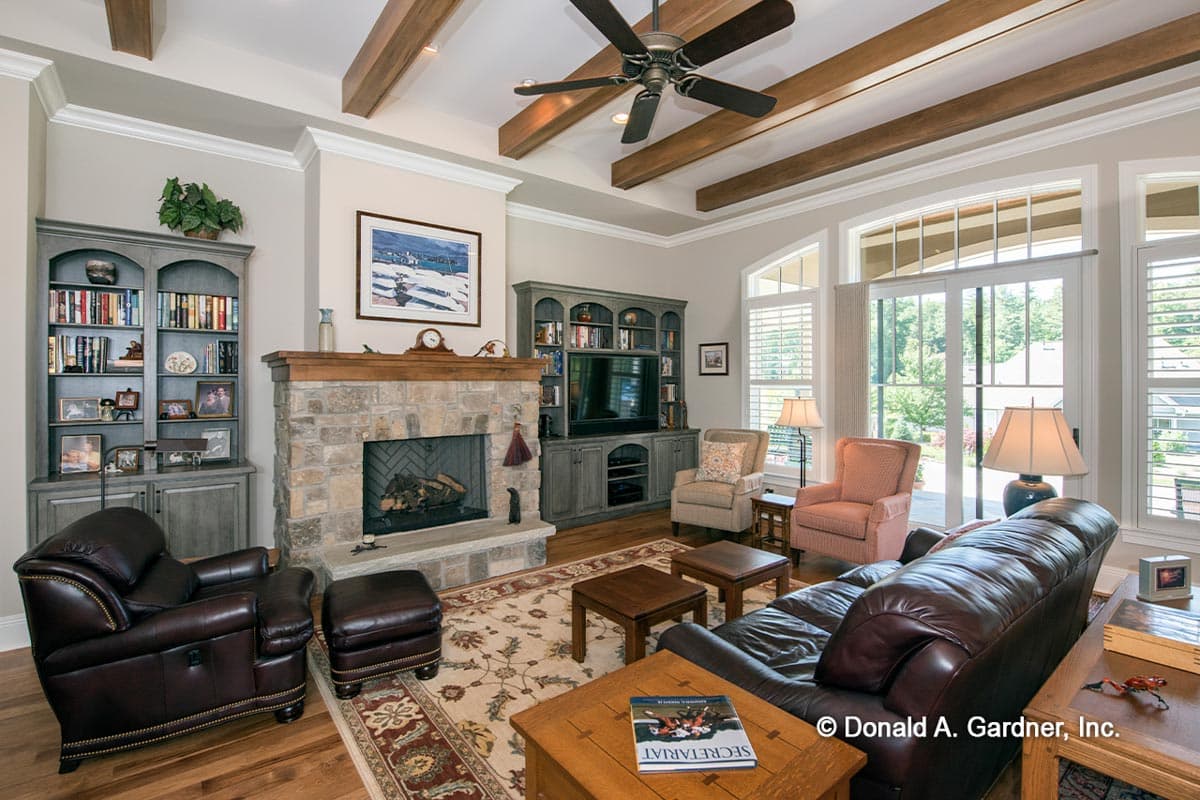 Great room with stone fireplace, built-in bookshelves, exposed wood ceiling beams, and large windows.